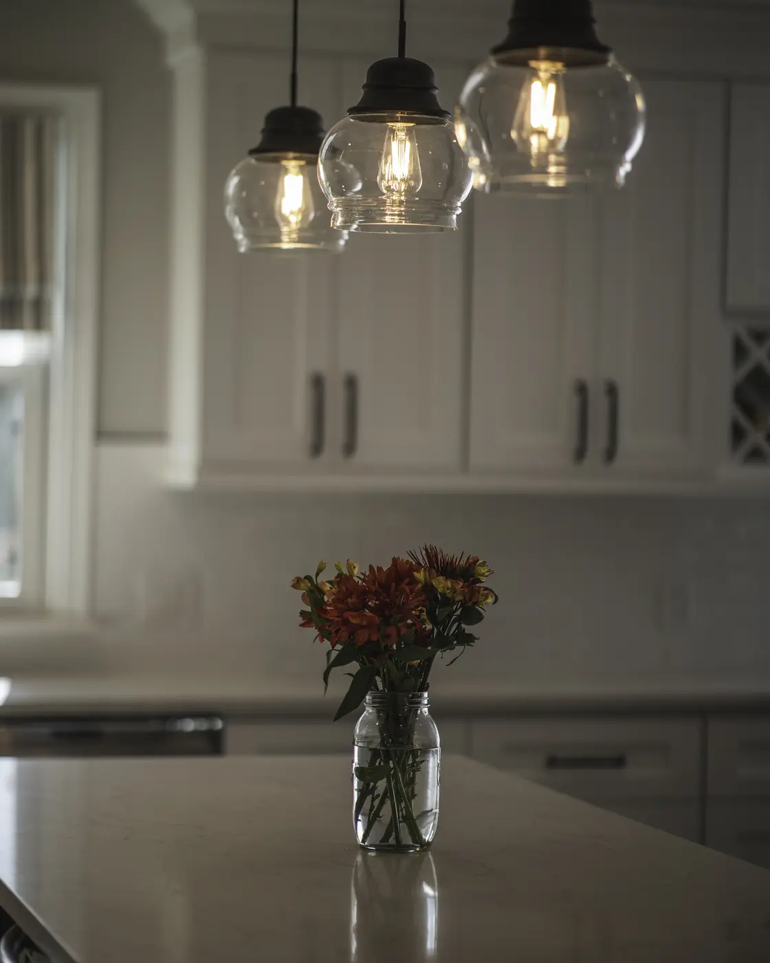 Three glass pendant lights above a kitchen island with white countertop and fresh flowers