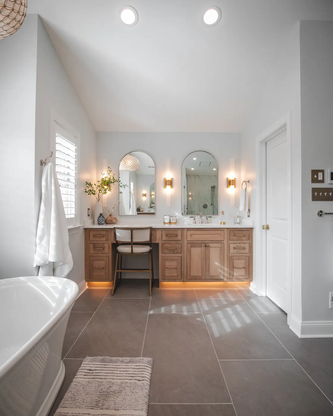 Elegant bathroom with a floating light wood vanity, dual arched mirrors, and under-cabinet lighting