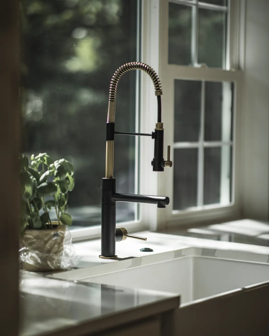 Close-up of matte black and gold pull-down faucet above a white farmhouse sink