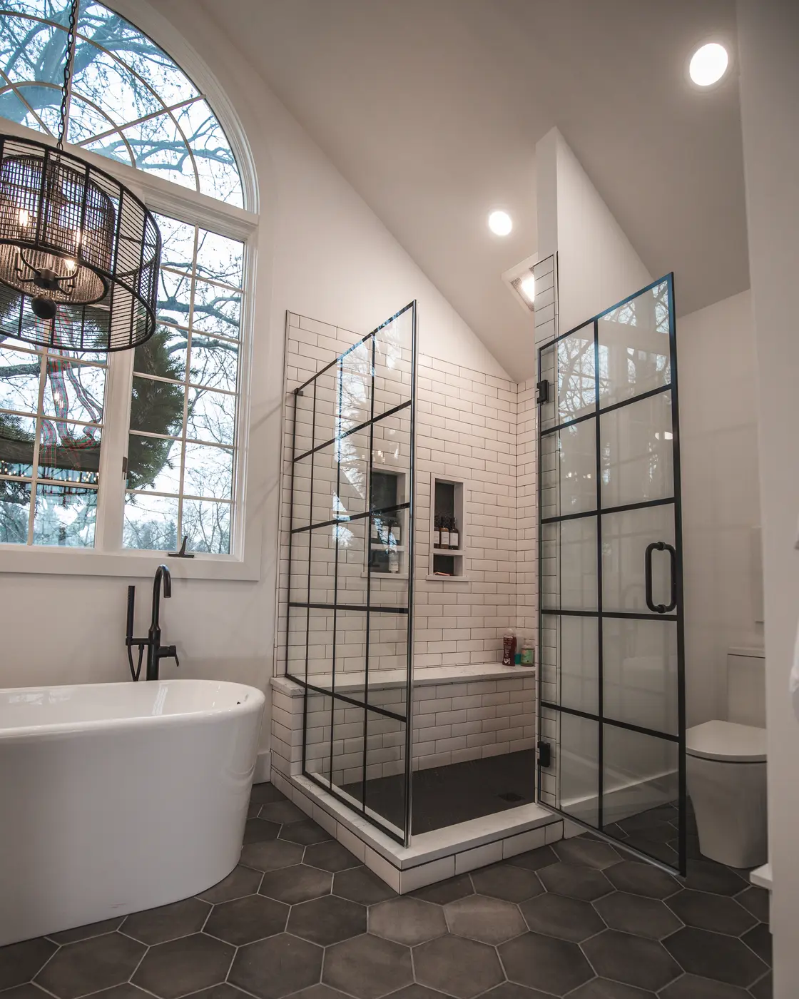 Spacious bathroom with black grid glass shower, white tile, and freestanding tub